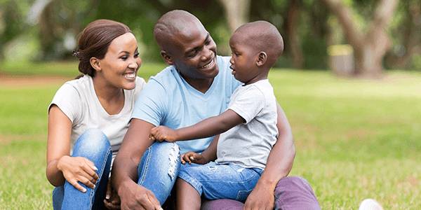 Man and woman with toddler on their lap sitting in the grass